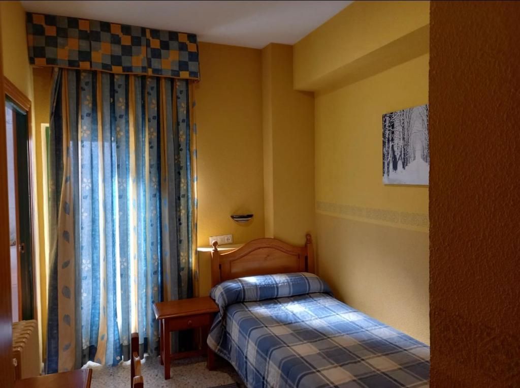 Pequeño dormitorio amarillo con una cama individual, ropa de cama a cuadros azules y cortinas de rayas azules.