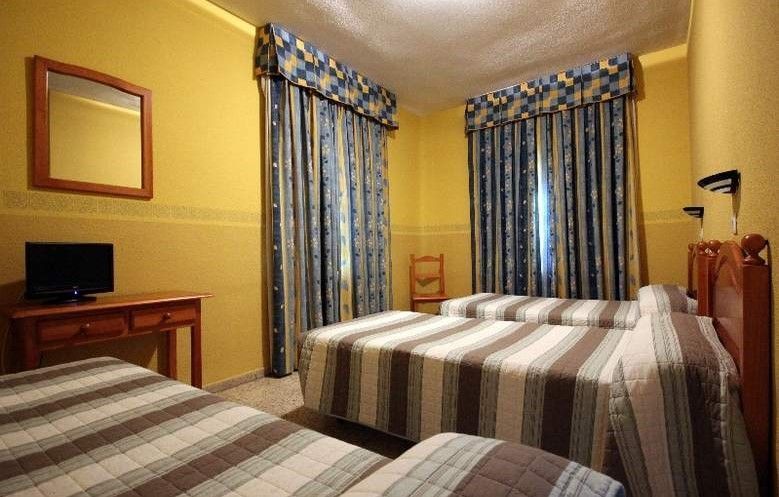 Habitación de hotel con tres camas individuales, paredes amarillas, cortinas de rayas azules y muebles de madera.