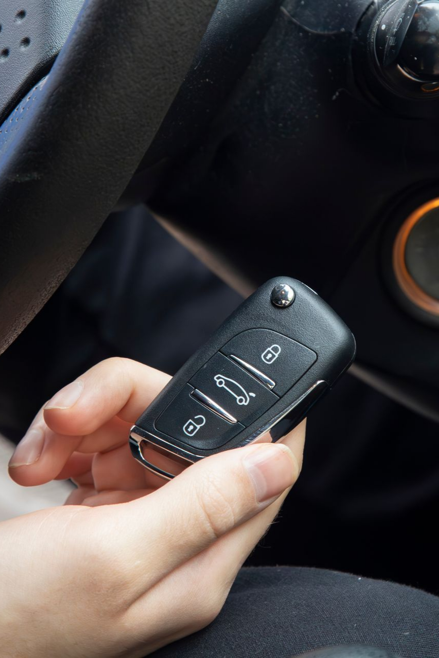 La main d'une personne tenant une clé de voiture noire près du tableau de bord d'un véhicule, avec des boutons de verrouillage/déverrouillage.