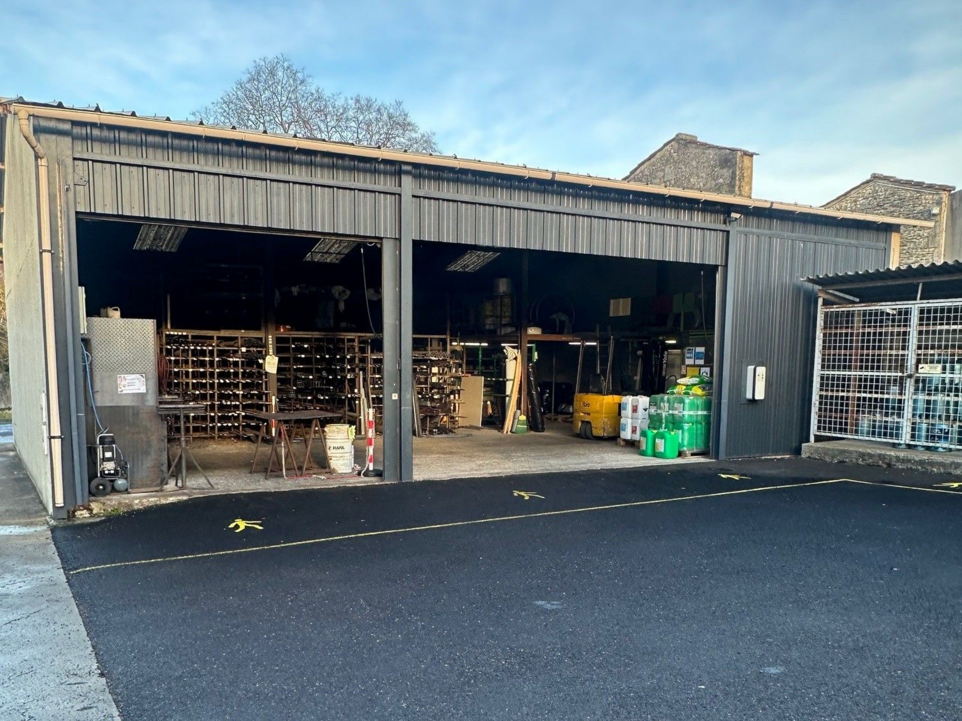 Hangar gris foncé à travées ouvertes, rempli d'équipements industriels, sur une surface d'asphalte noir.