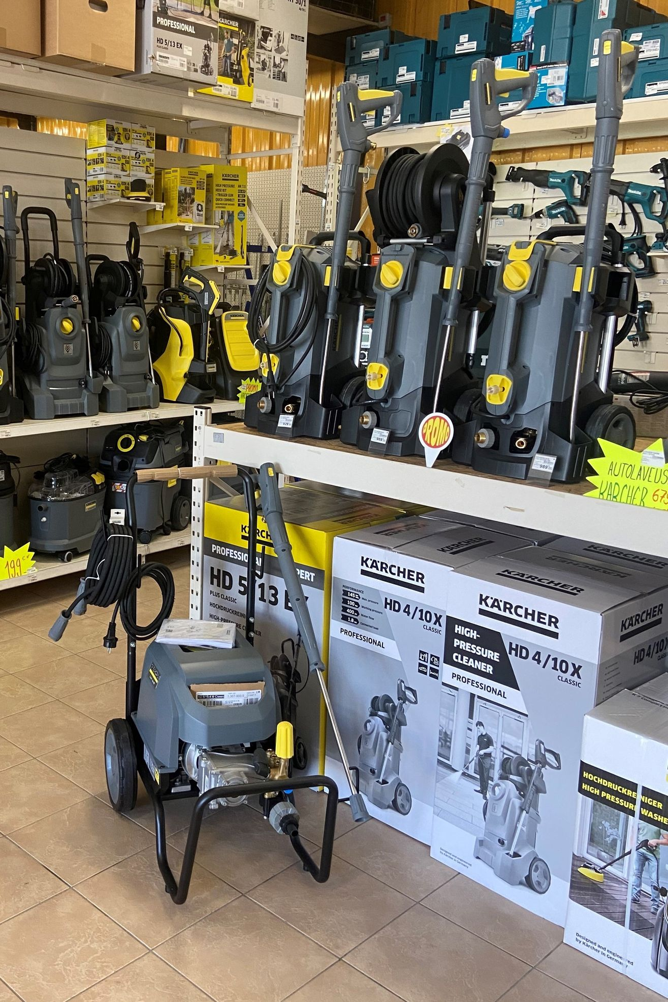 Des nettoyeurs haute pression sont exposés dans un magasin. Des appareils gris et jaunes sont disposés sur des étagères et au sol.