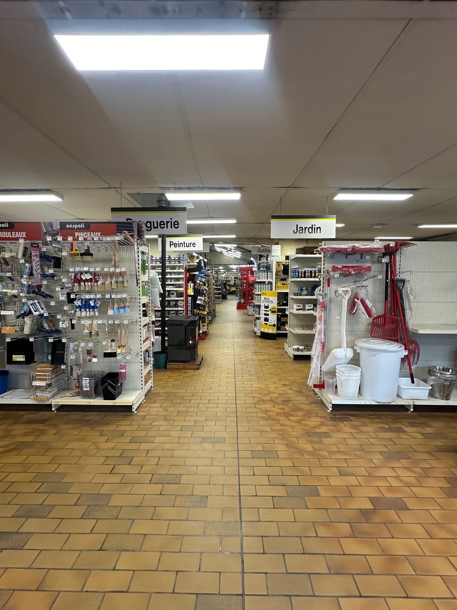 Intérieur d'une quincaillerie avec des allées d'étagères remplies d'outils et de fournitures sous une lumière fluorescente vive.