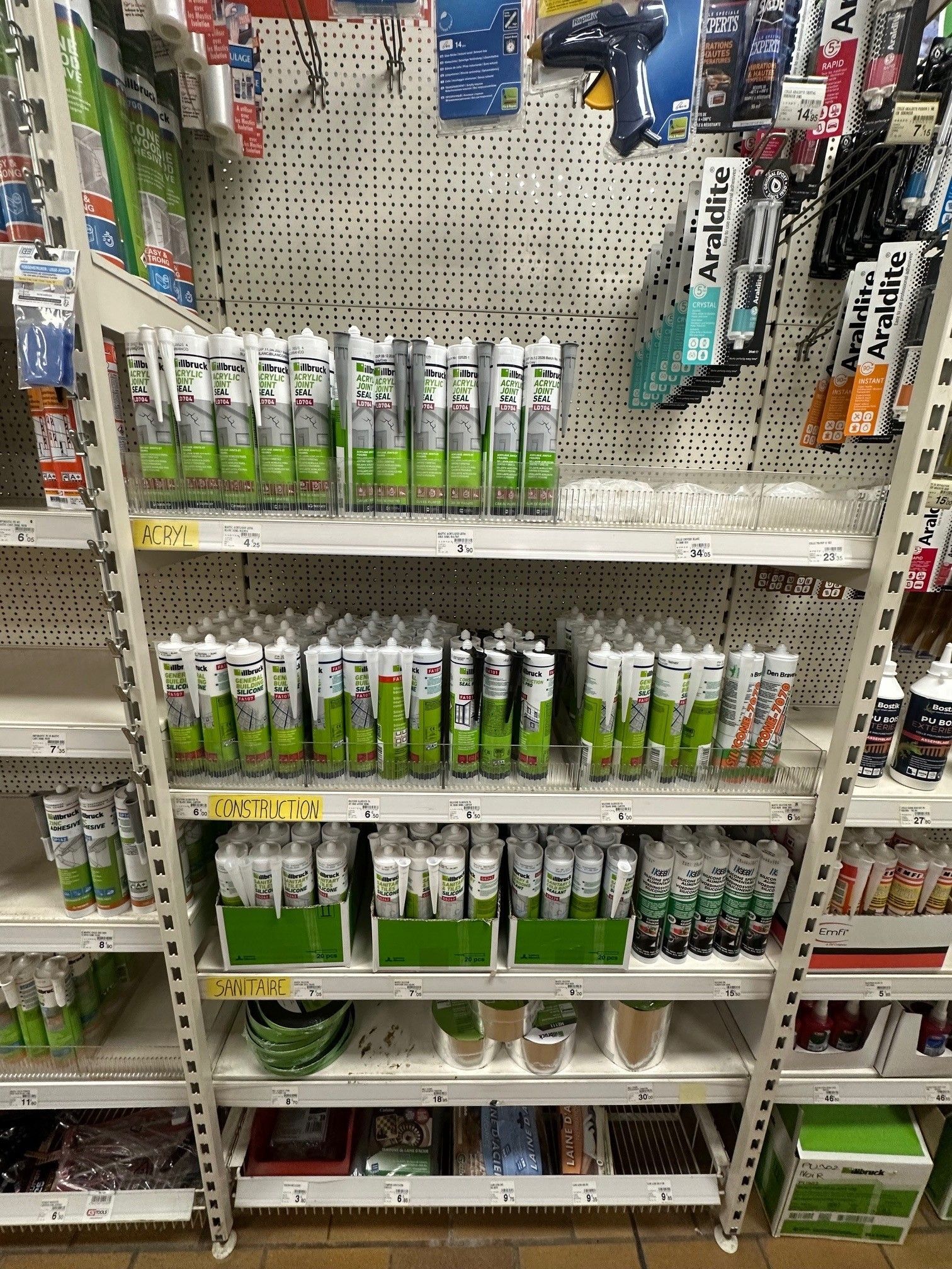 Des rayons remplis de tubes de mastic verts et blancs de différentes couleurs dans un magasin.