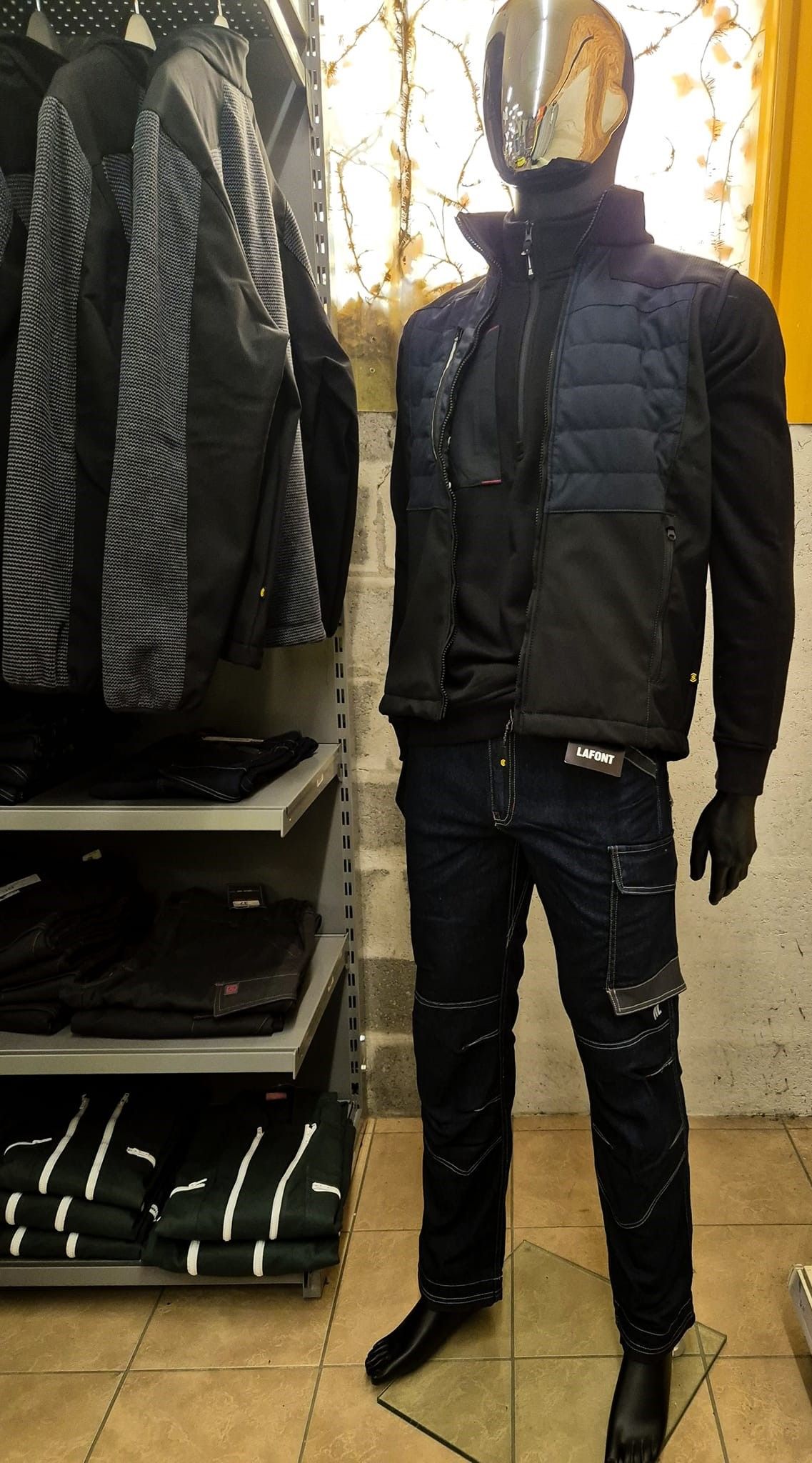 Mannequin en tenue noire : gilet matelassé, jean et chemise noire, dans un magasin de vêtements.