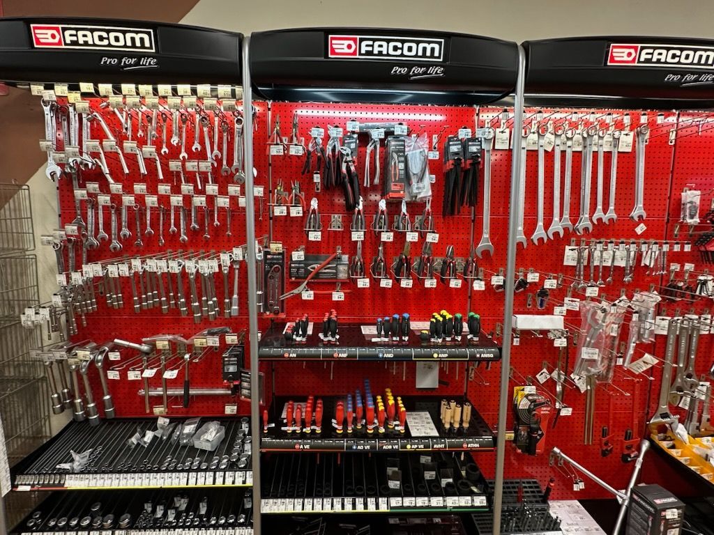 Présentoir à outils avec divers outils à main, notamment des clés, des pinces et des tournevis, sur fond rouge.