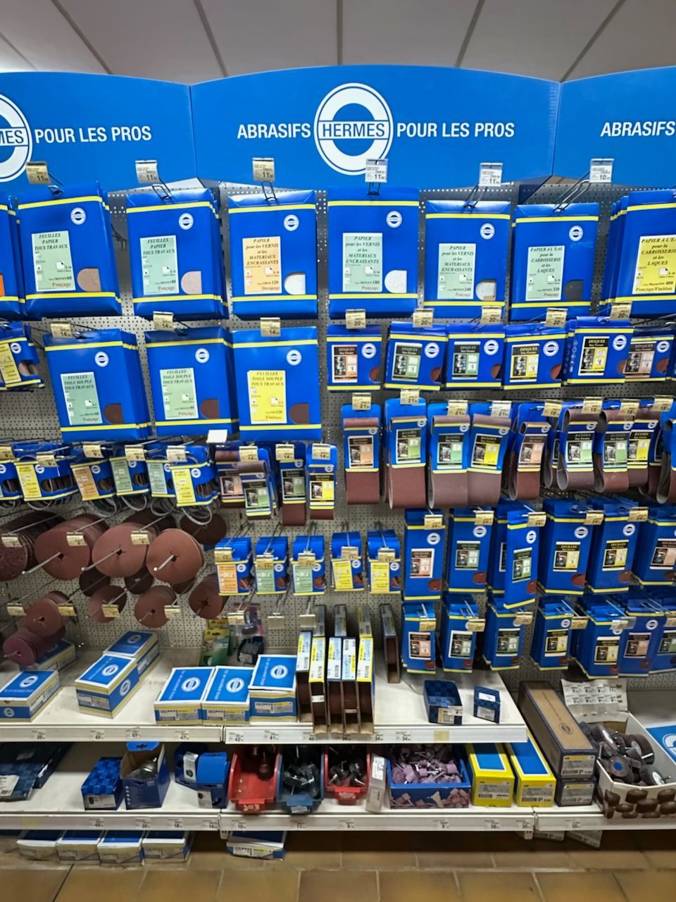 Présentoir d'outils abrasifs dans une quincaillerie ; les emballages bleus dominent.