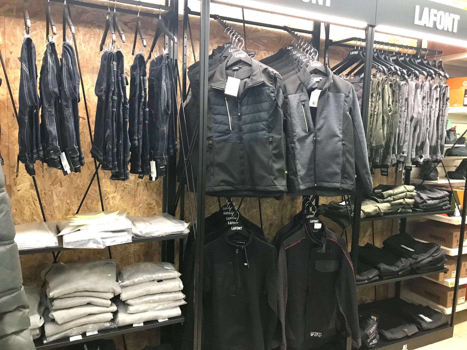 Présentoir de vêtements avec vestes, pantalons et pulls noirs dans un magasin.