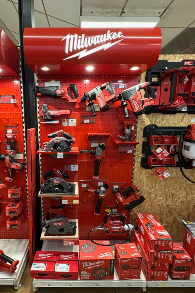 Présentoir d'outils électriques Milwaukee dans un magasin ; outils rouges sur un panneau perforé rouge.