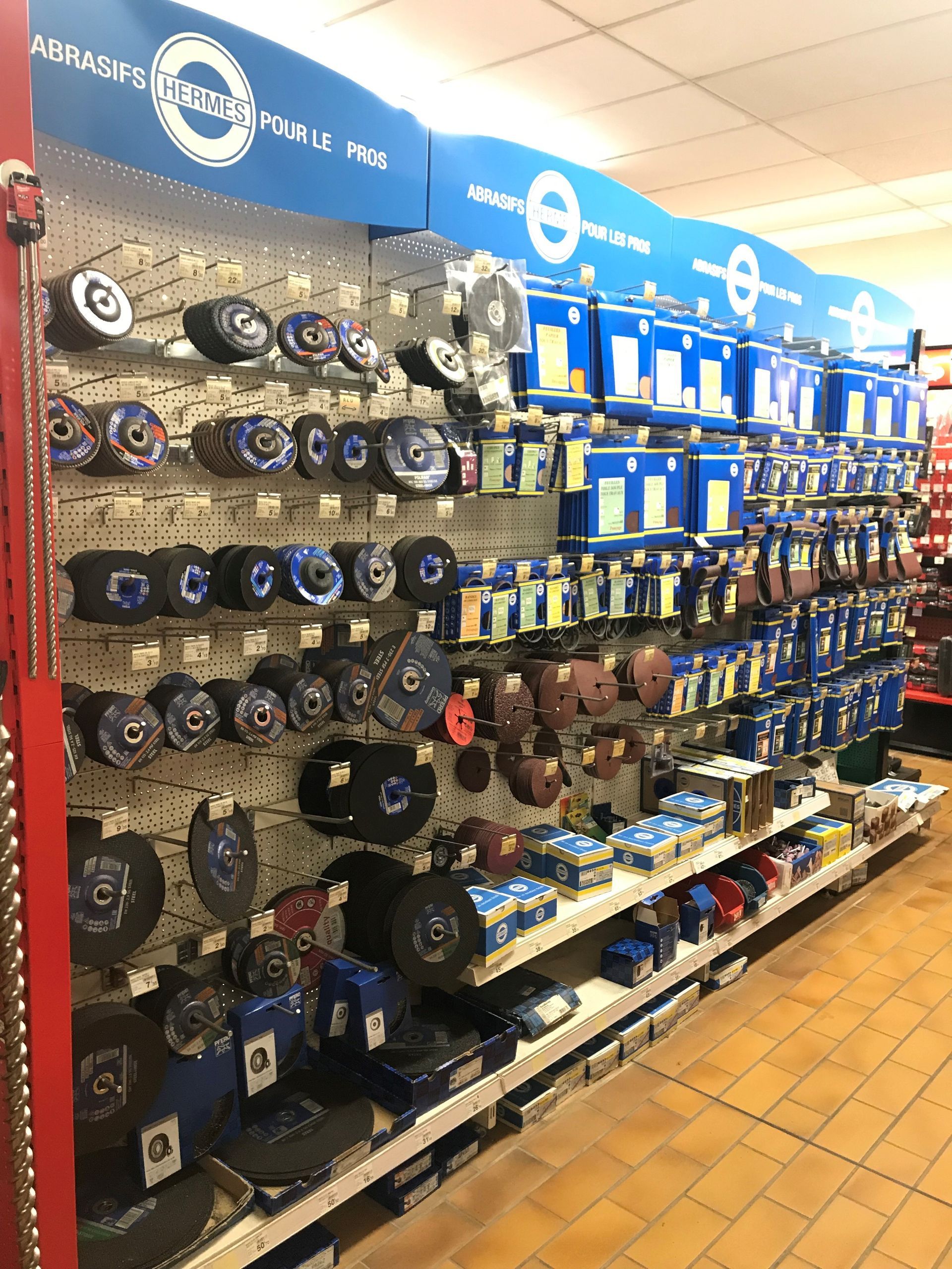 Des étagères remplies de disques abrasifs et de meules dans une quincaillerie. La marque, aux couleurs bleues et blanches, est bien visible.