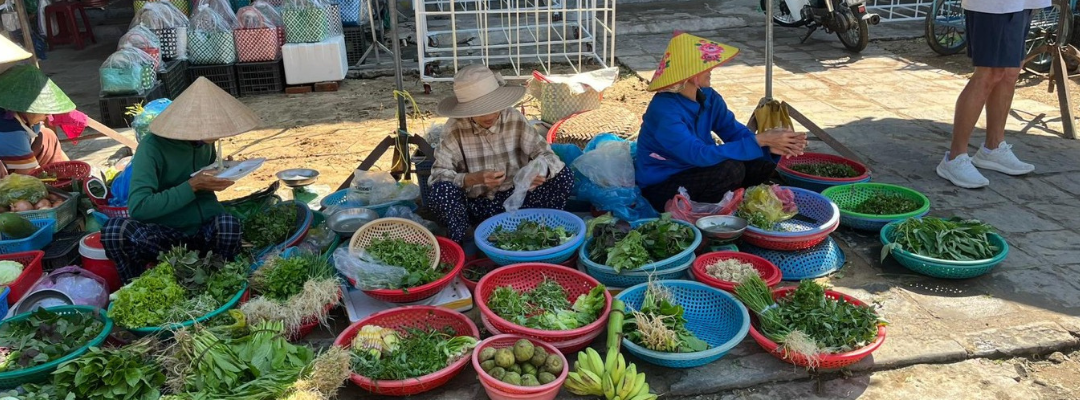 A group of women are sitting on the ground selling vegetables at a market.