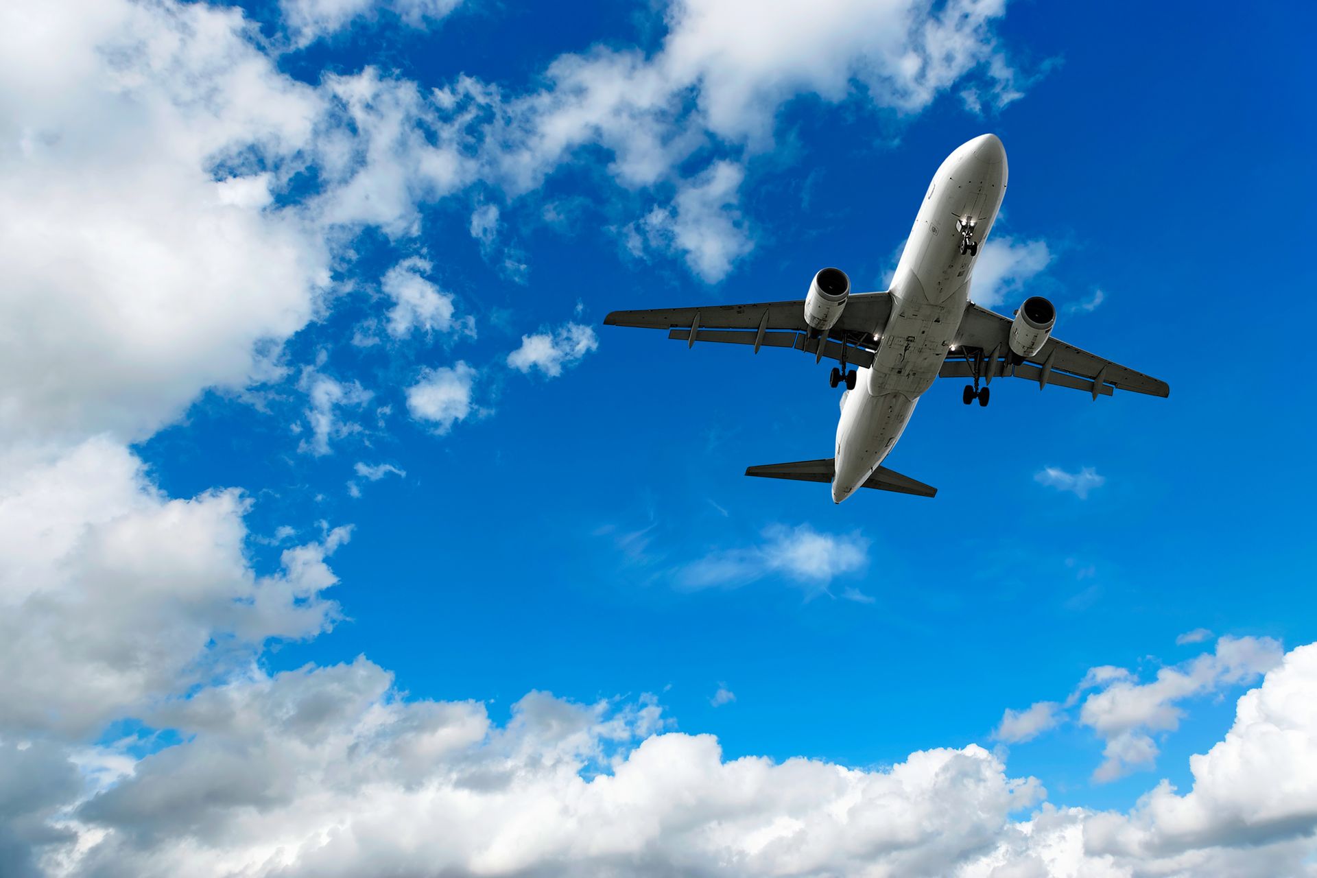 Airplane in flight against a bright blue sky with fluffy white clouds.