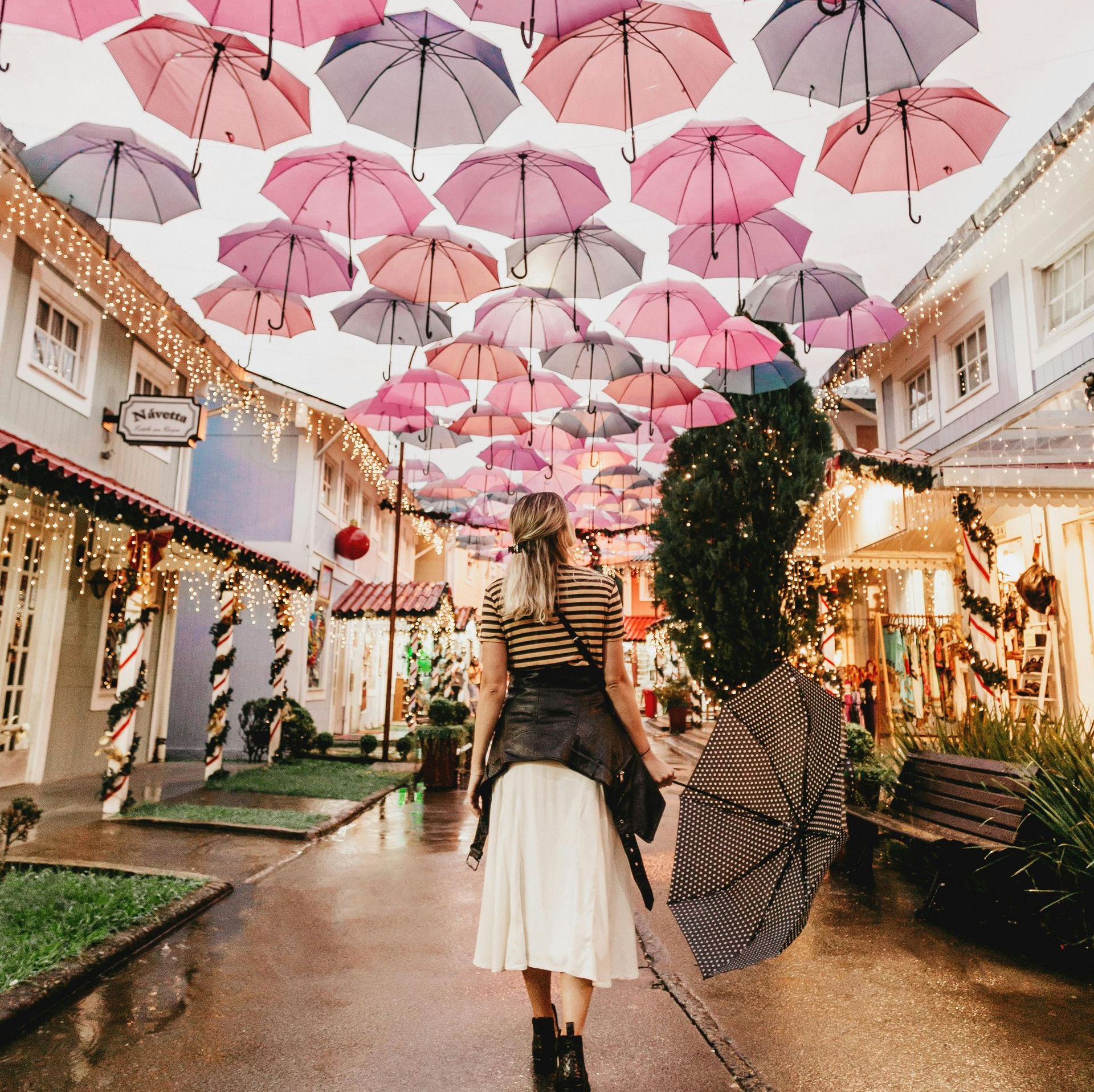 Woman walking down a street protected by multiple umbrellas overhead.