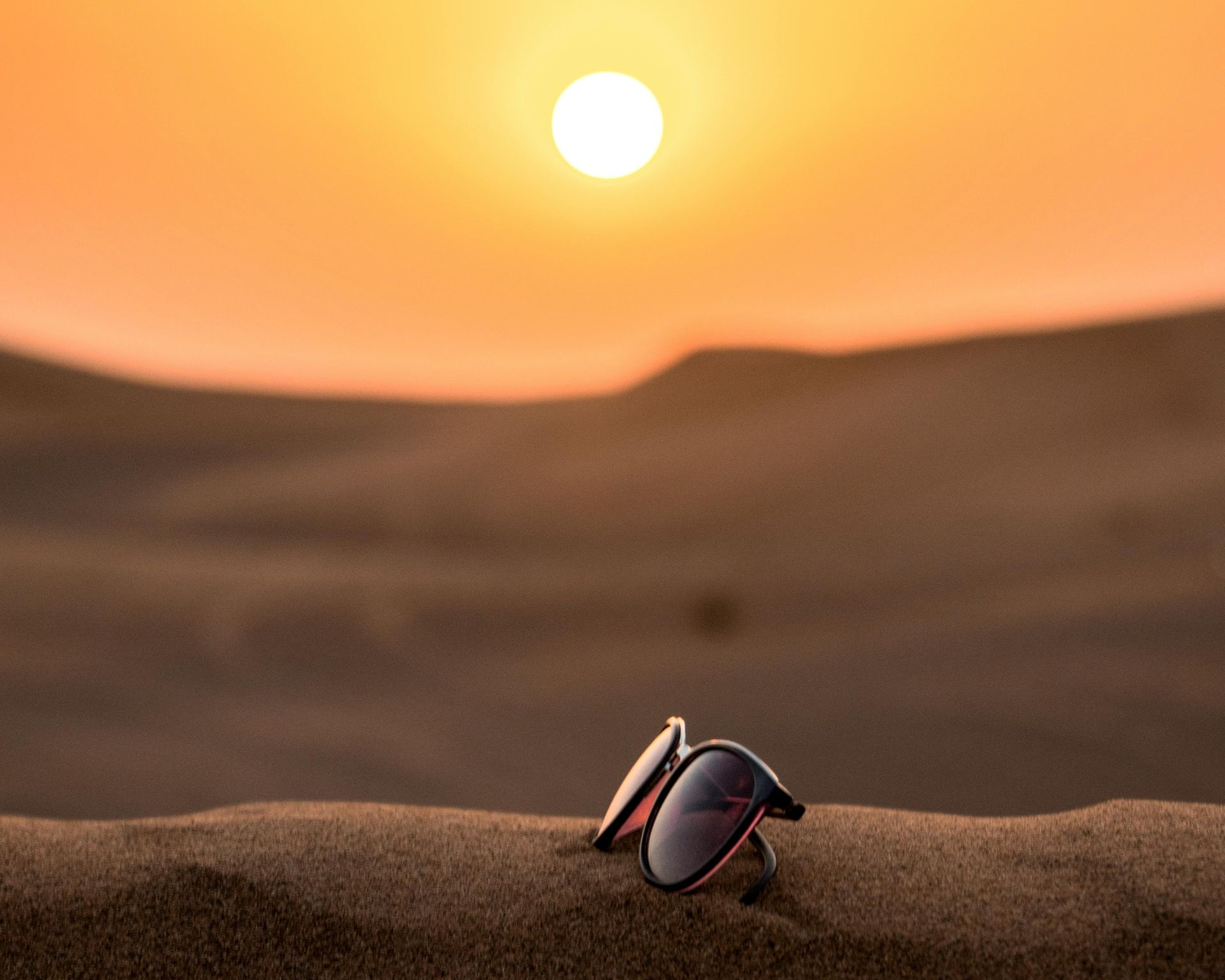 Sunglasses in sand, sunset in the background. Desert landscape, warm colors.