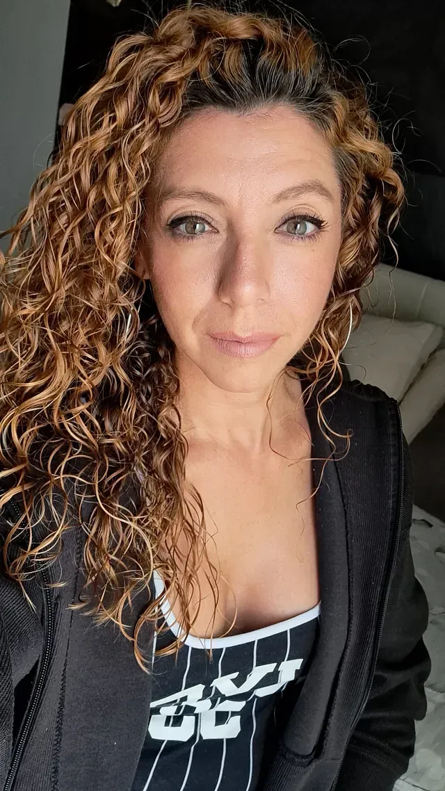 Una mujer con cabello rizado se está tomando un selfie en un dormitorio.