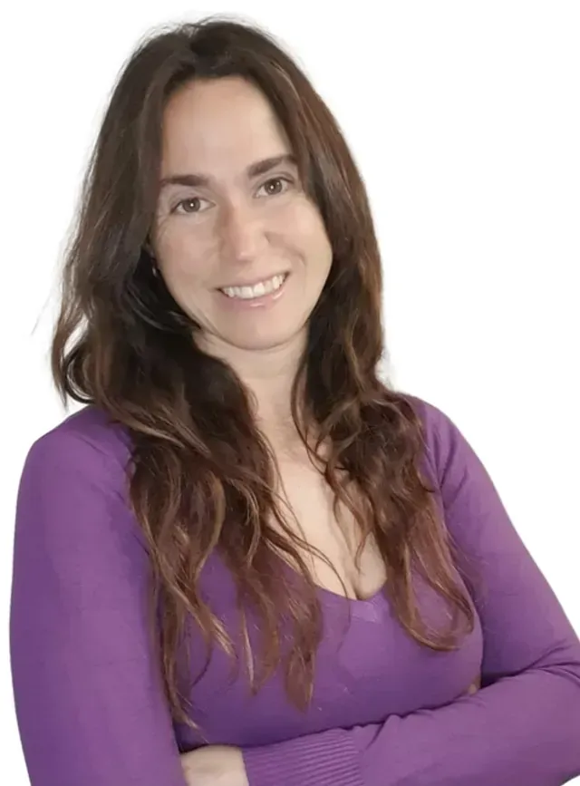 Una mujer con una camisa morada sonríe con los brazos cruzados.