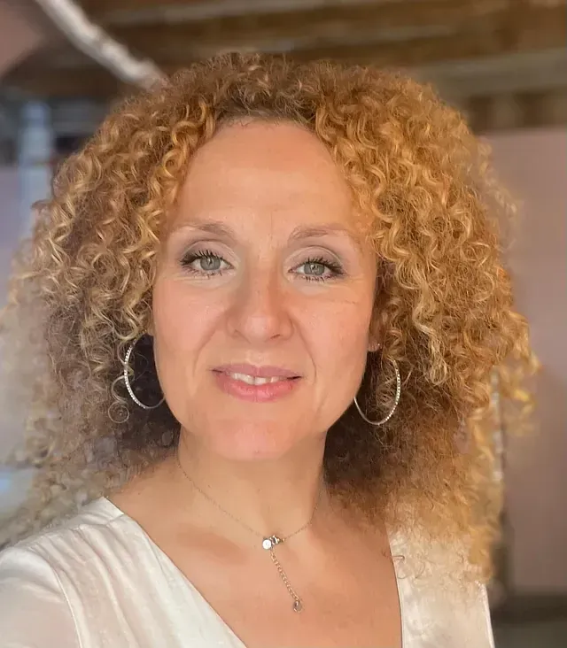 Una mujer con cabello rizado lleva una camisa blanca y pendientes.