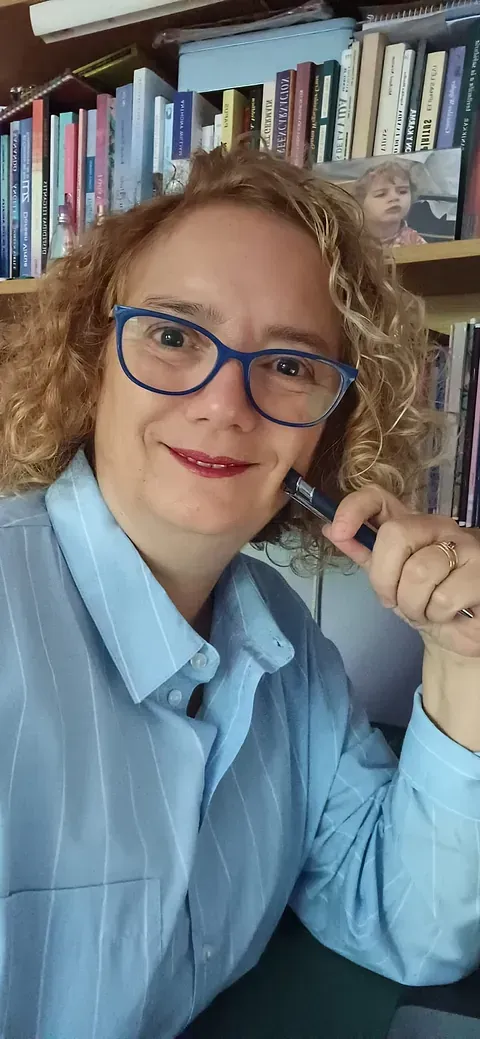 Una mujer que lleva gafas y una camisa azul está sentada frente a una estantería.