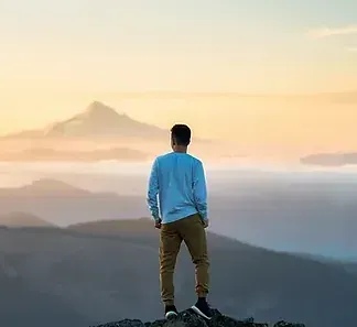 Un hombre está parado en la cima de una montaña mirando la puesta de sol.