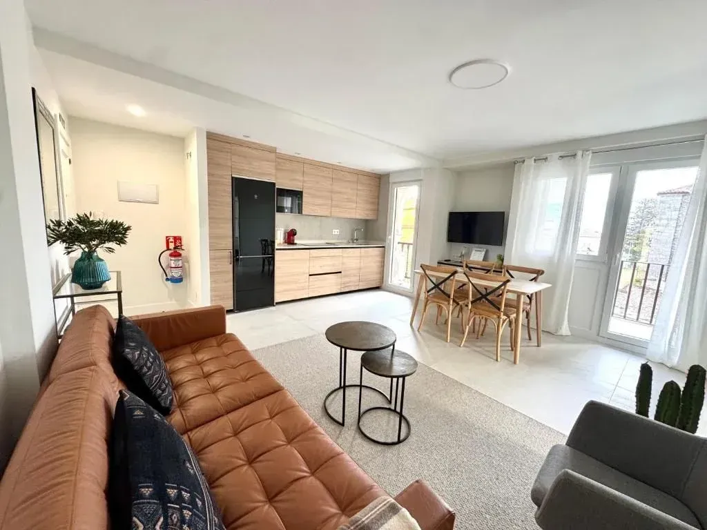 Moderna sala de estar con cocina. Sofá de cuero marrón, mesa de comedor y armarios de madera clara.