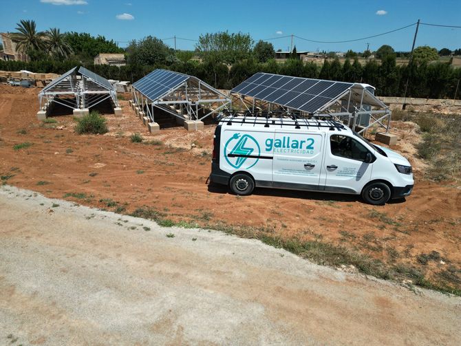 Una furgoneta blanca está estacionada delante de una fila de paneles solares.