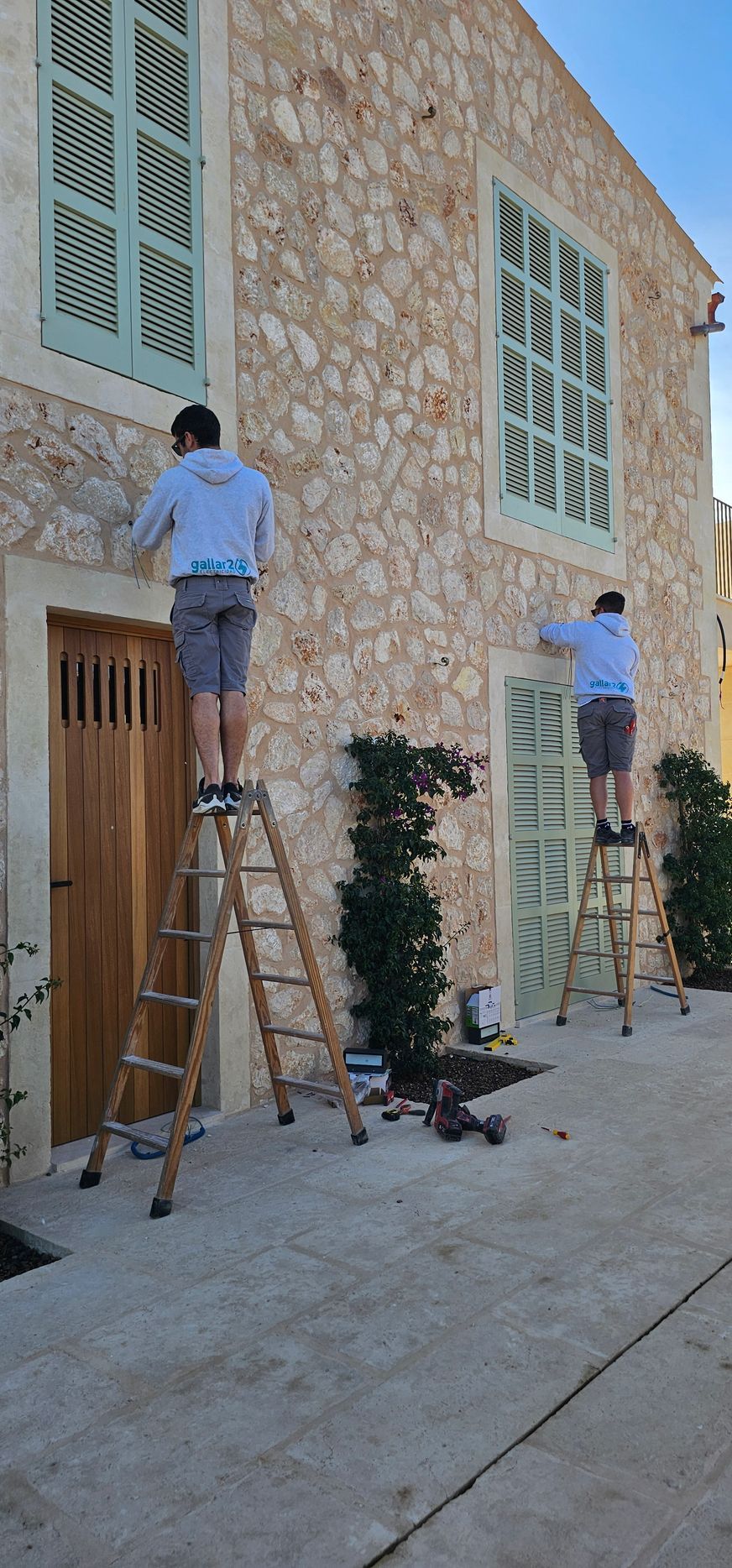 Dos hombres están de pie sobre escaleras pintando un edificio de piedra.