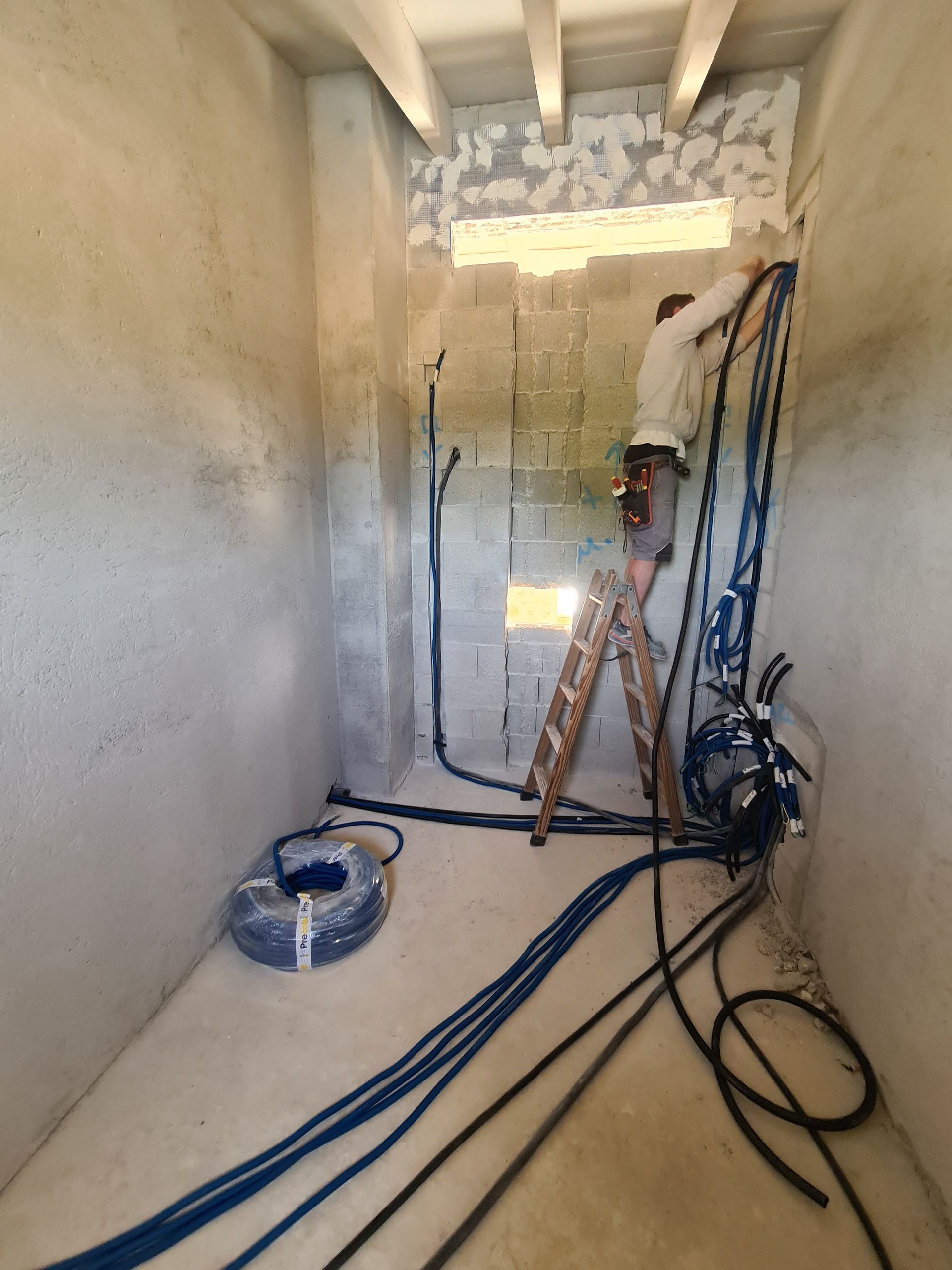 Un hombre está parado en una escalera en una habitación con muchos cables.