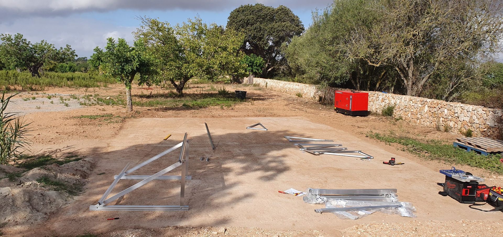 Se está construyendo una valla en un campo de tierra con árboles al fondo.