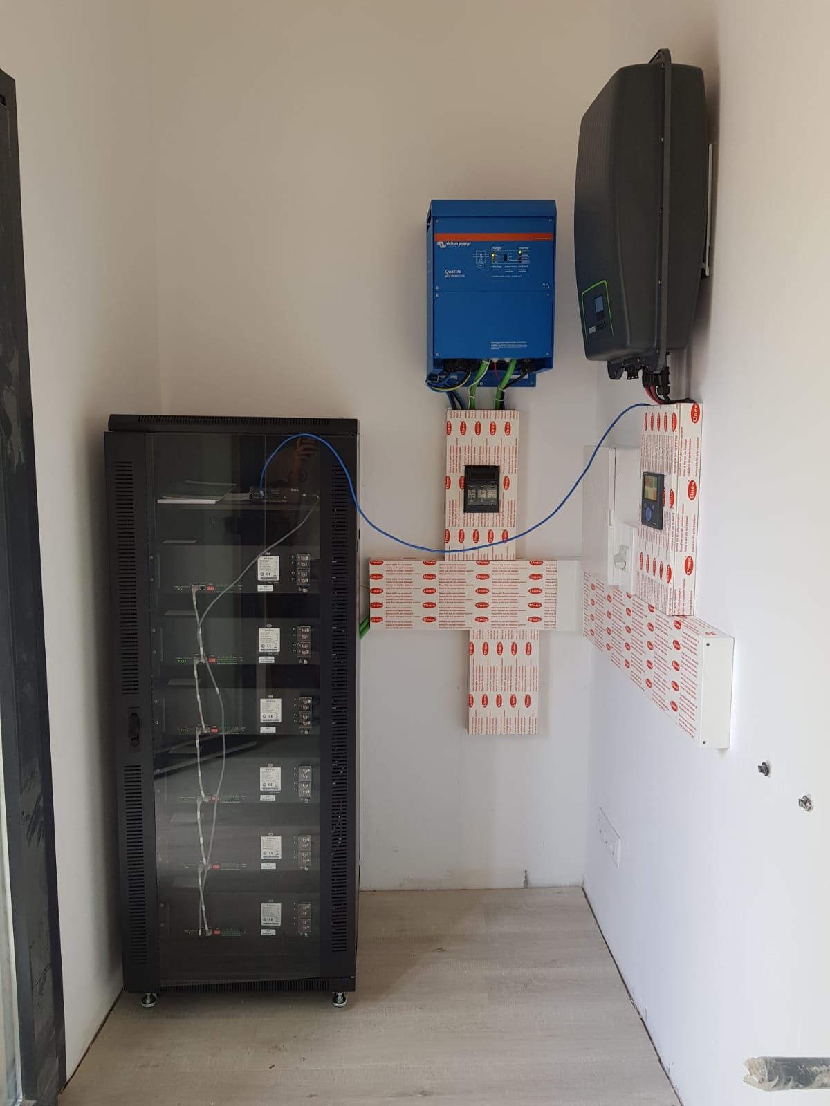 Una habitación con un armario negro y un inversor azul en la pared.