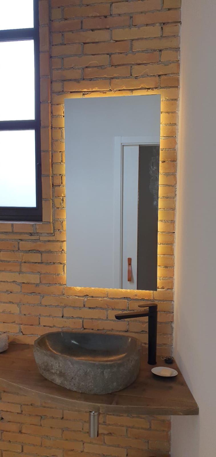 Un baño con lavabo, espejo y pared de ladrillo.