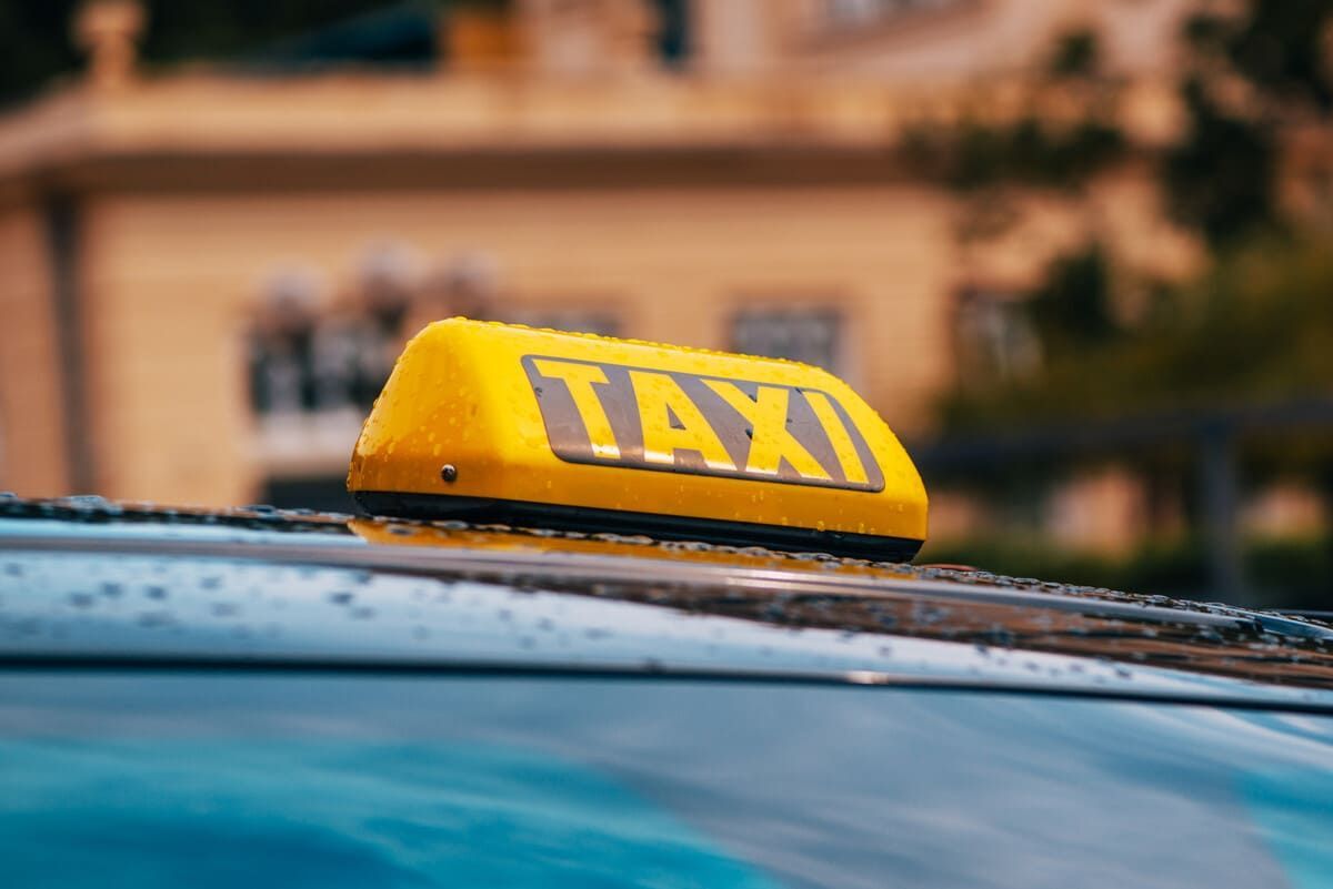 Letrero de taxi amarillo sobre el techo de un automóvil, contra un fondo de edificio borroso.