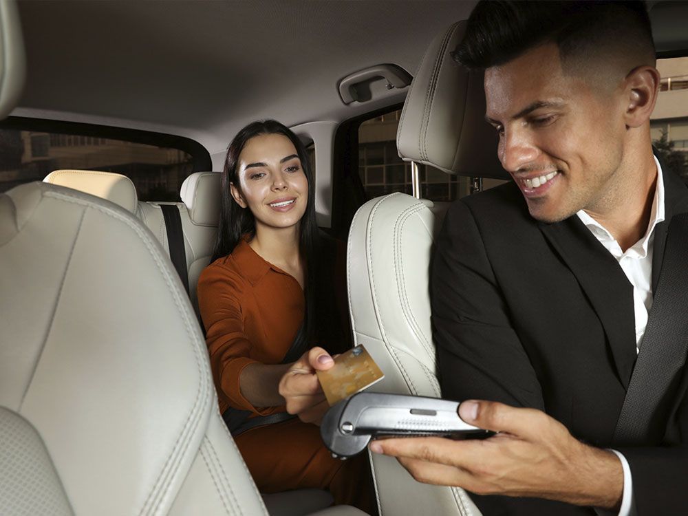 Una mujer en un coche usa un lector de tarjetas que sostiene un hombre, ambos sonriendo. Dentro de un vehículo.