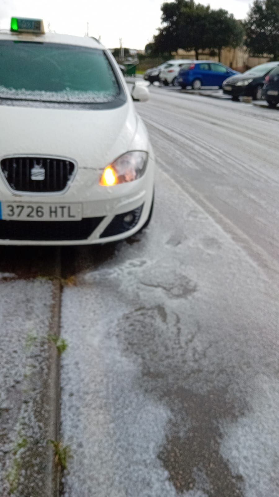 Taxi blanco en una calle cubierta de granizo; la señal de giro a la derecha del vehículo está encendida.