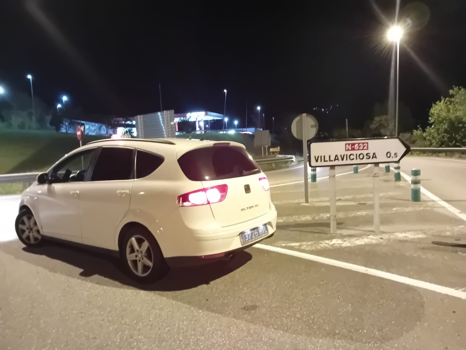 Coche blanco aparcado de noche junto a un cartel de Villaviciosa.