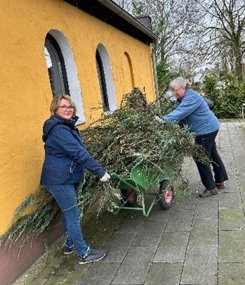 Zwei Frauen schieben eine Schubkarre voller Weihnachtsbäume.