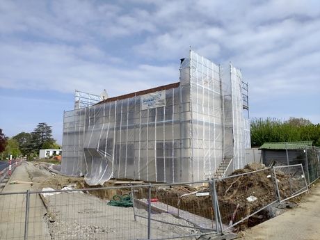 Un bâtiment est en cours de construction avec des échafaudages et une clôture autour.