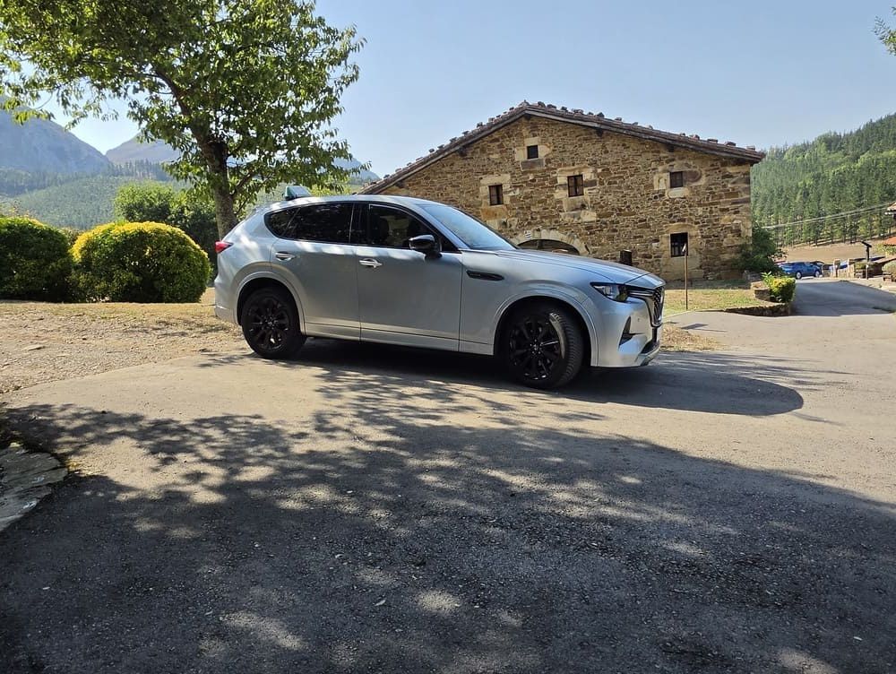 SUV plateado estacionado junto a una casa rústica de piedra en un entorno rural soleado.