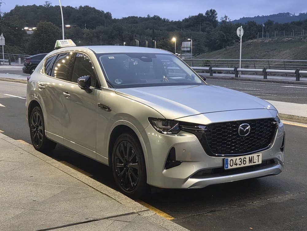 Un SUV Mazda plateado estacionado al borde de la carretera al anochecer, con montañas al fondo.