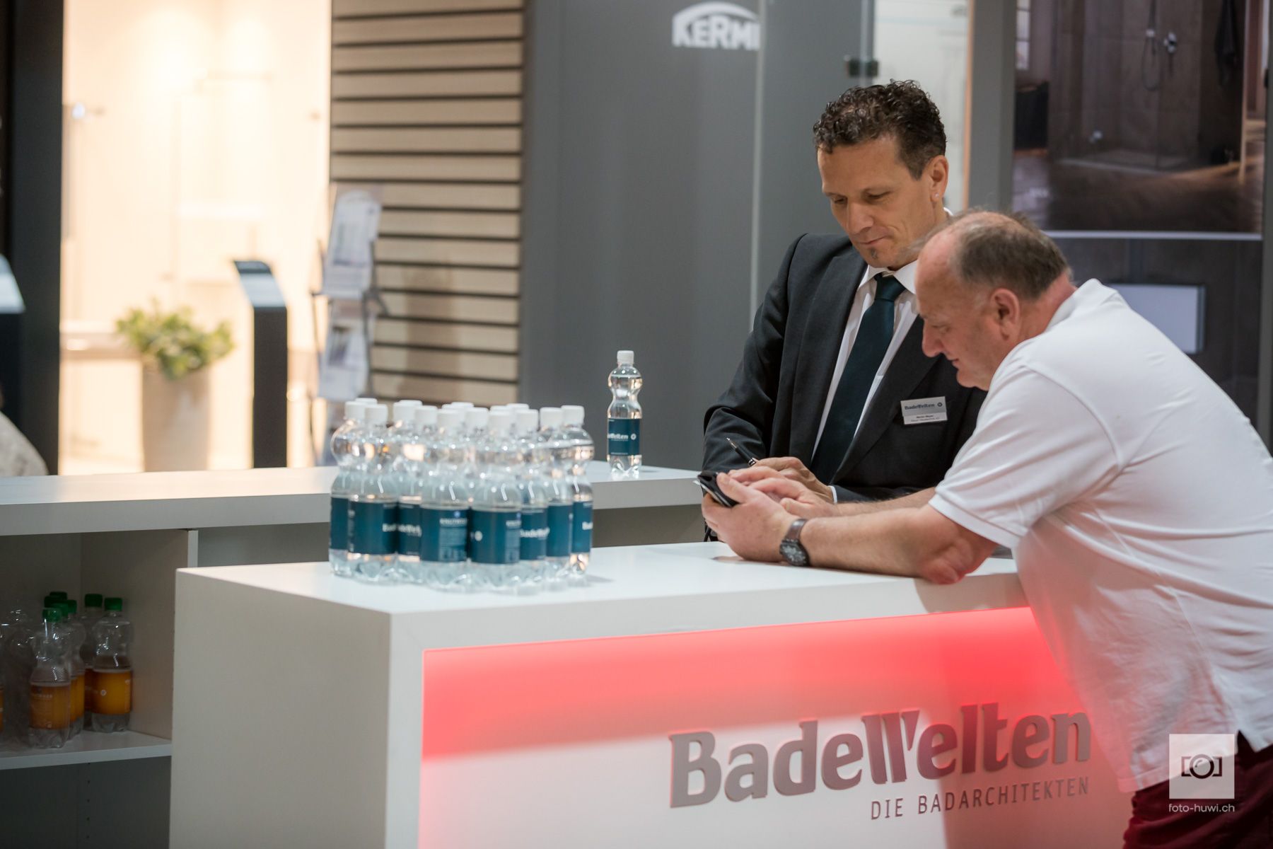 Zwei Männer sitzen an einem Tisch mit der Aufschrift „Badewelten“