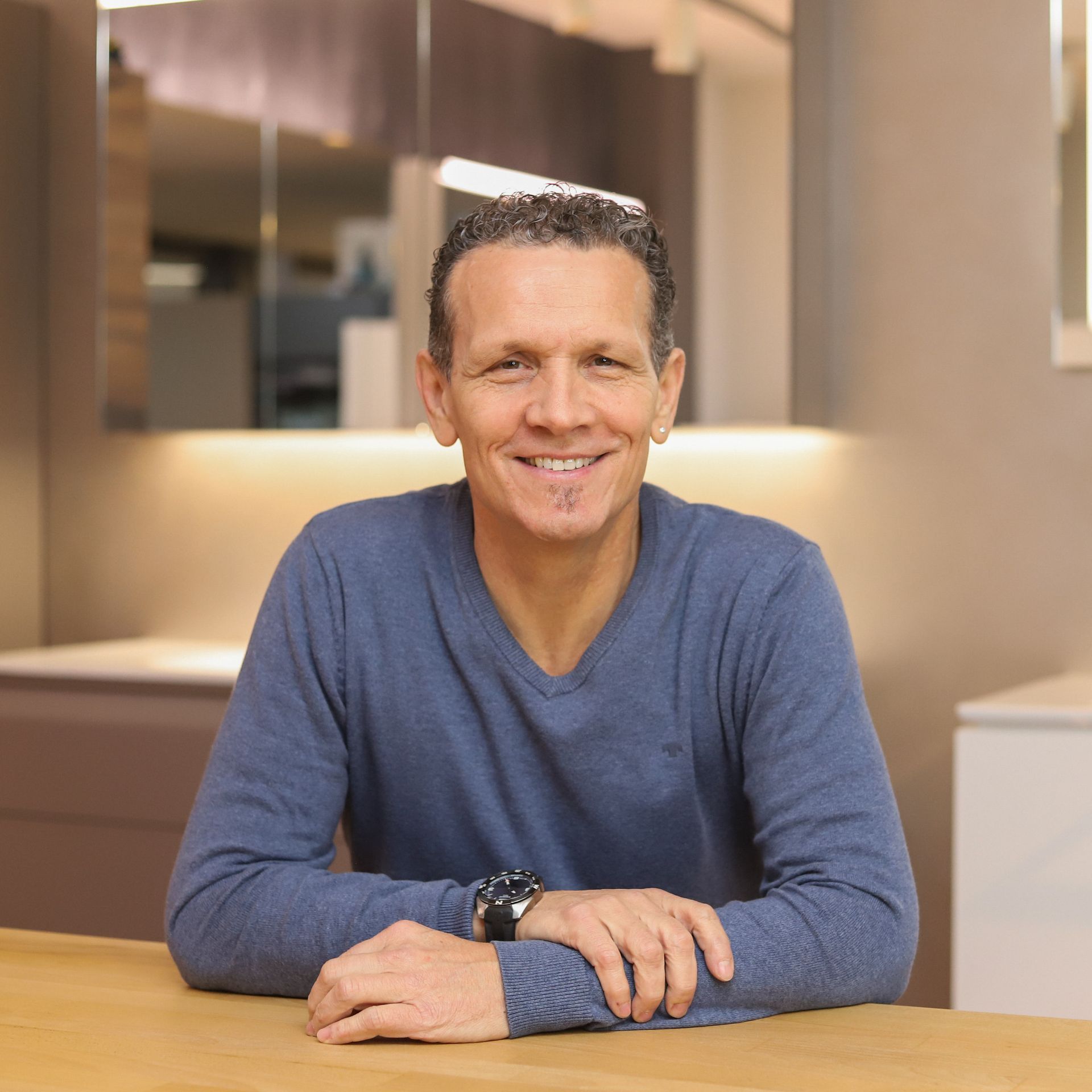 Ein Mann in einem blauen Pullover sitzt an einem Tisch