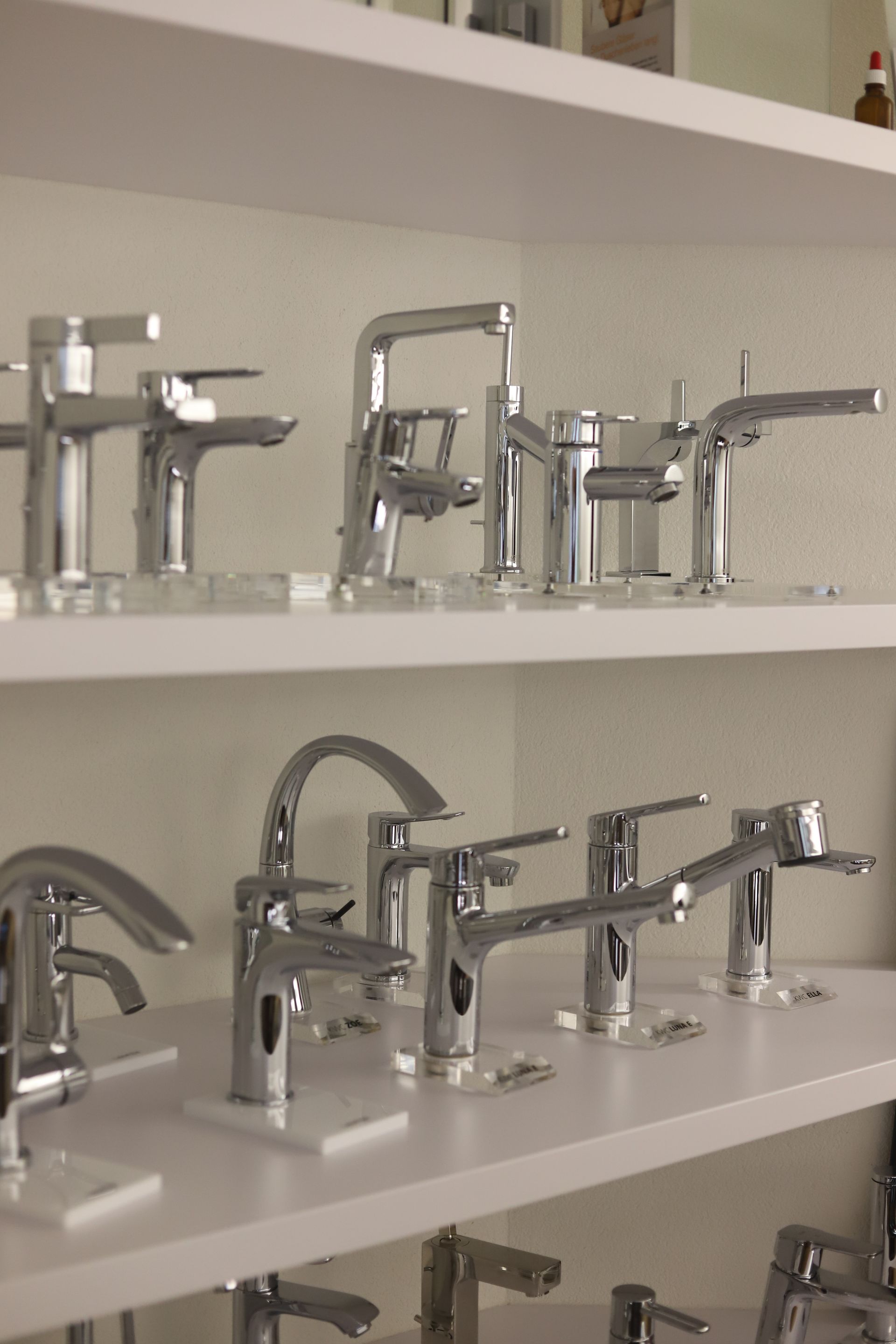 Eine Reihe verchromter Wasserhähne auf einem weißen Regal
