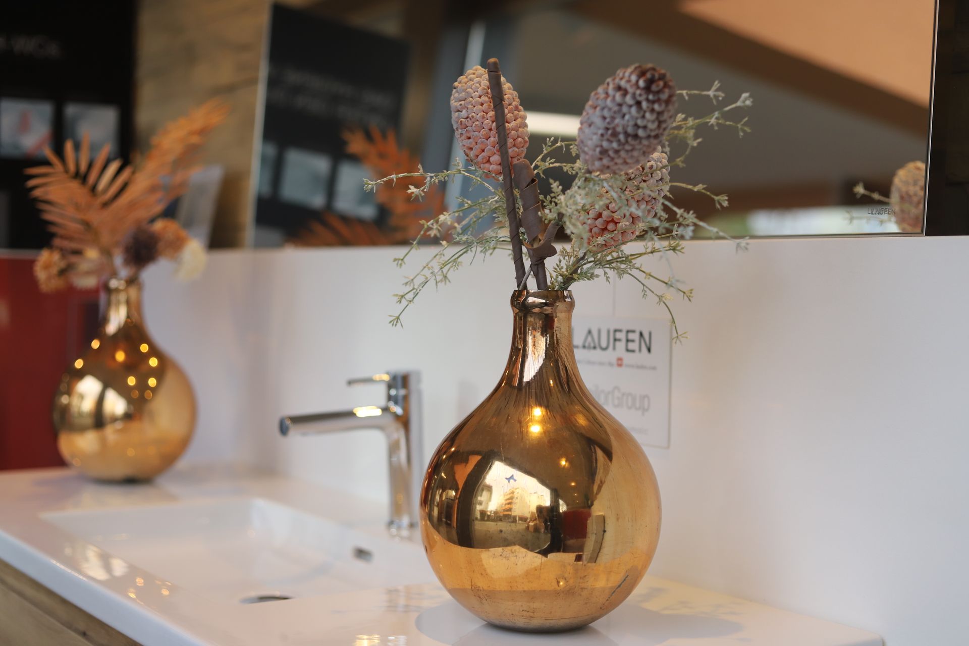 Eine goldene Vase mit Blumen darin steht auf einer Badezimmerablage