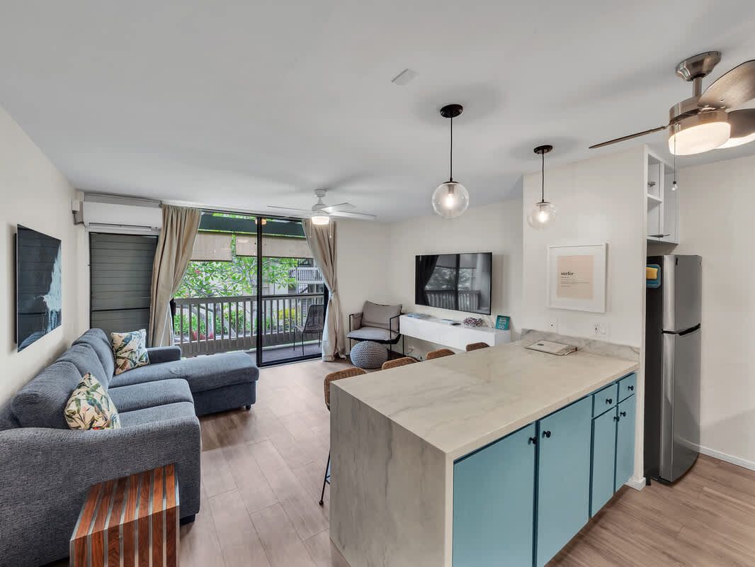 Living room with blue couch, kitchen island, and sliding door to balcony.