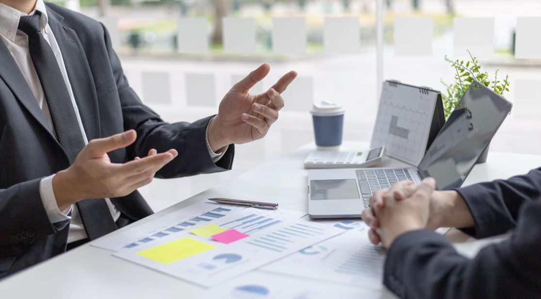 Dos profesionales con traje analizan gráficos y datos empresariales sobre un escritorio en una oficina luminosa.