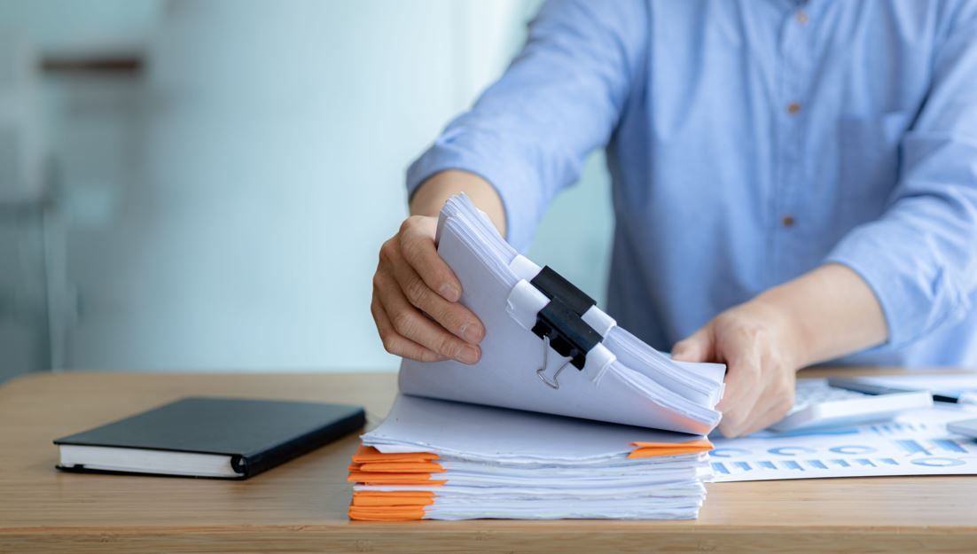 Una persona con una camisa azul claro revisa una pila de documentos