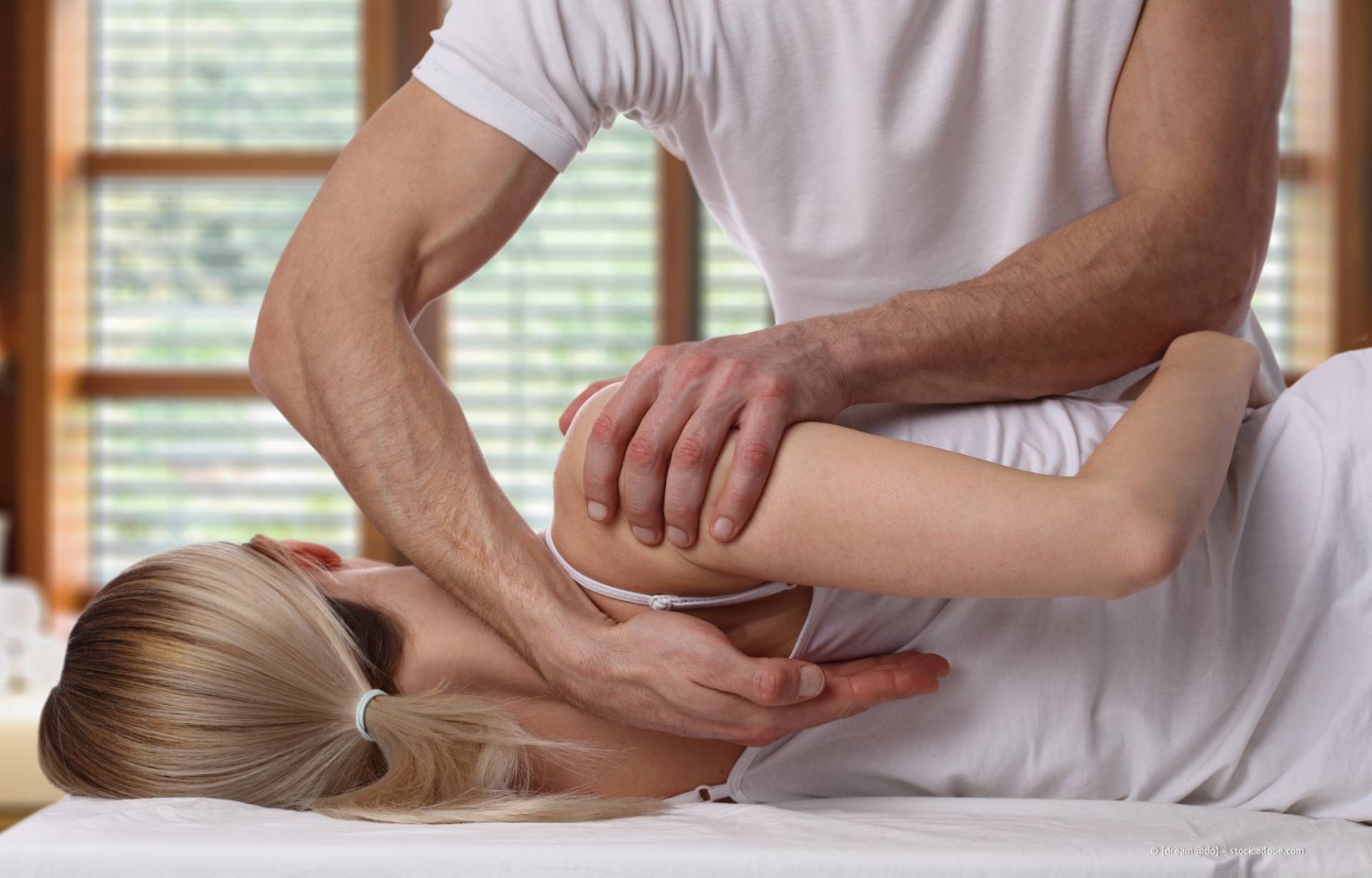 Eine Person, die Physiotherapie erhält; der Therapeut manipuliert den Arm und die Schulter des Patienten.