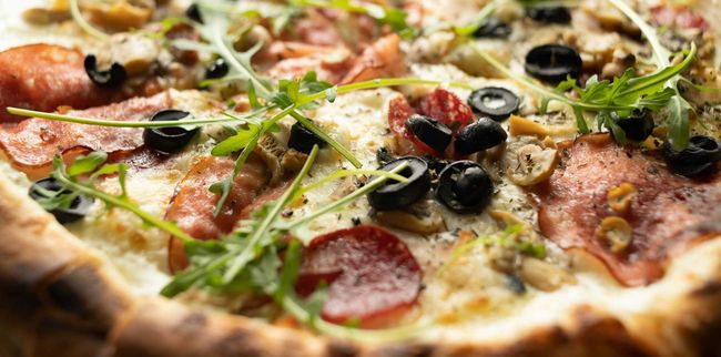 Un primer plano de una pizza con pepperoni, aceitunas y champiñones sobre una mesa.