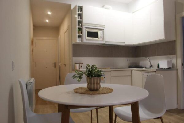 Una pequeña mesa de comedor redonda y blanca, con una planta en maceta 