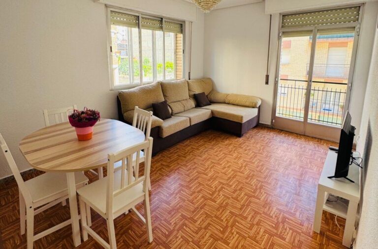 Una sala de estar con paredes claras y suelo de parqué, que cuenta con un sofá 