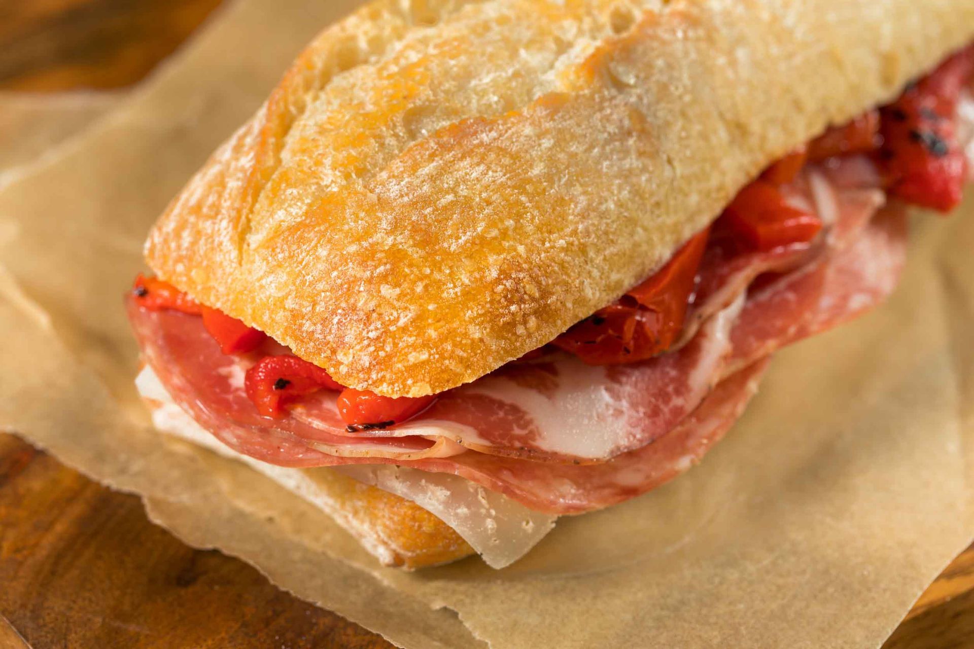 Un primer plano de un sándwich en un trozo de papel sobre una mesa de madera.