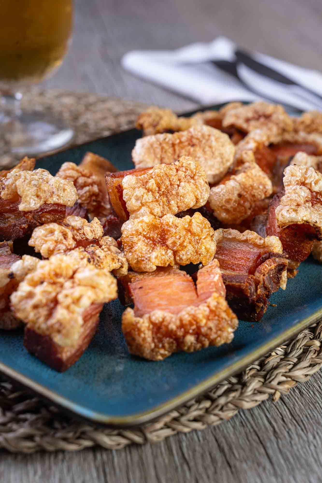 Un plato de cerdo frito en una mesa de madera junto a un vaso de cerveza.